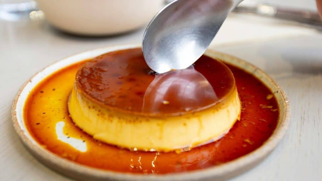 Creamy caramel flan dessert with caramel sauce on a white plate.
