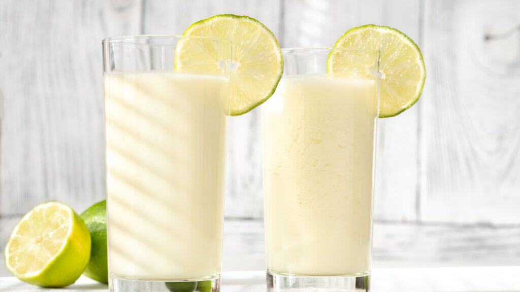 Two glasses of lemon juice with lemon slices on a white wooden background.